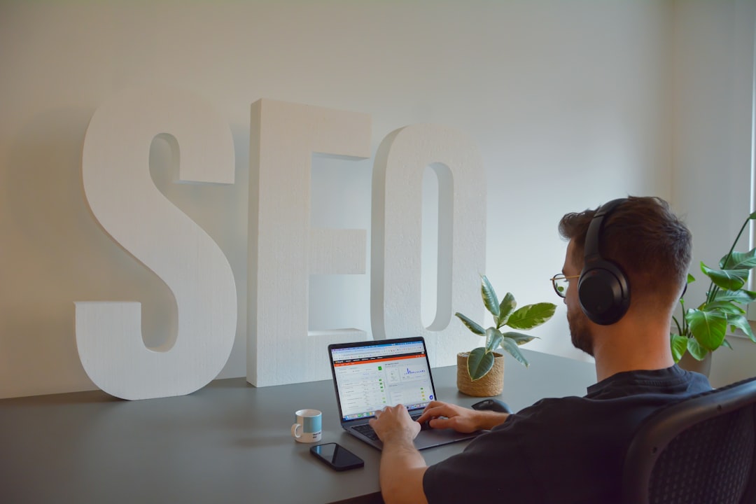 Focused professional working at an SEO agency, seated at a modern office desk. He is wearing headphones to stay concentrated, with large SEO letters in the background emphasizing the digital environment. On the desk, there is a cup of espresso, a mobile phone, and a small plant, adding a touch of greenery to the workspace.